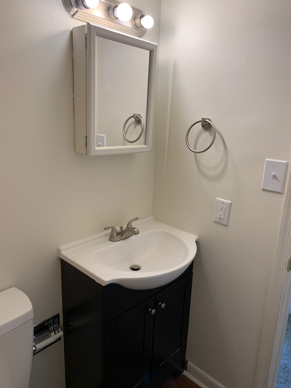 A Taneytown Village bathroom with a dark vanity, a white sink, a mirrored medicine cabinet, and a vanity light