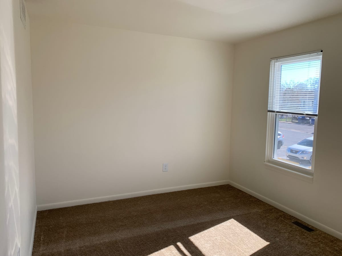 A carpeted Taneytown Village bedroom with neutral walls and a window over the parking area