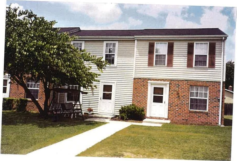 A Taneytown Village townhouse with a shade tree, bench swing, and green lawn out front