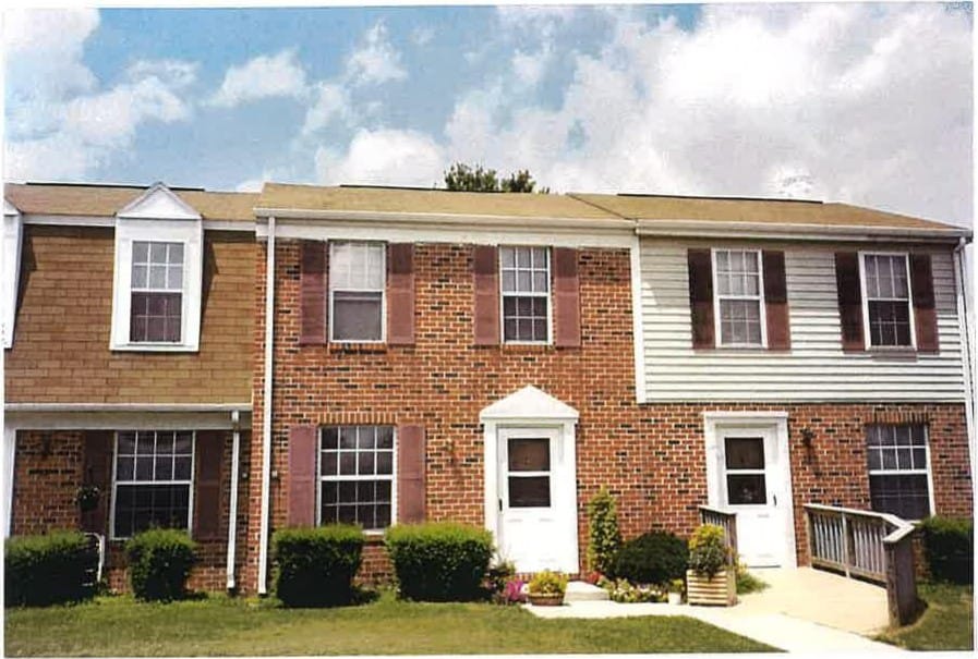 A row of brick Taneytown Village townhouses with white doors and flowers by the walkway