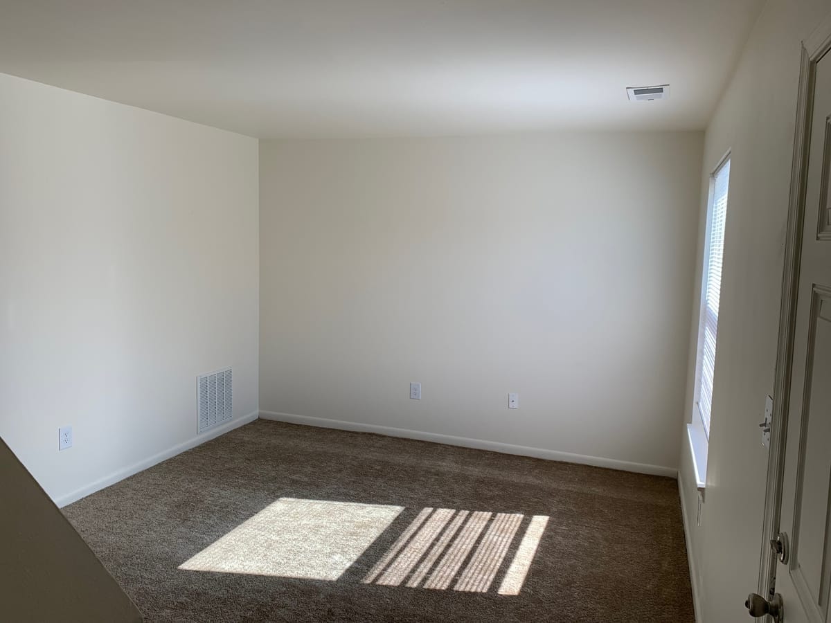 A carpeted Taneytown Village living room with neutral walls and a bright window
