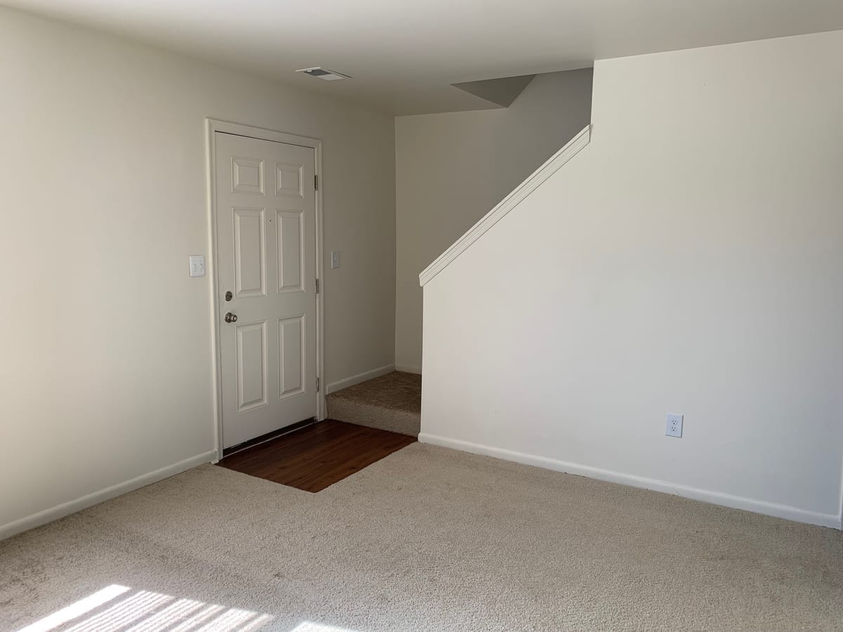 The living room of a Taneytown Village townhouse, with the front entry door and a carpeted staircase up to the bedrooms